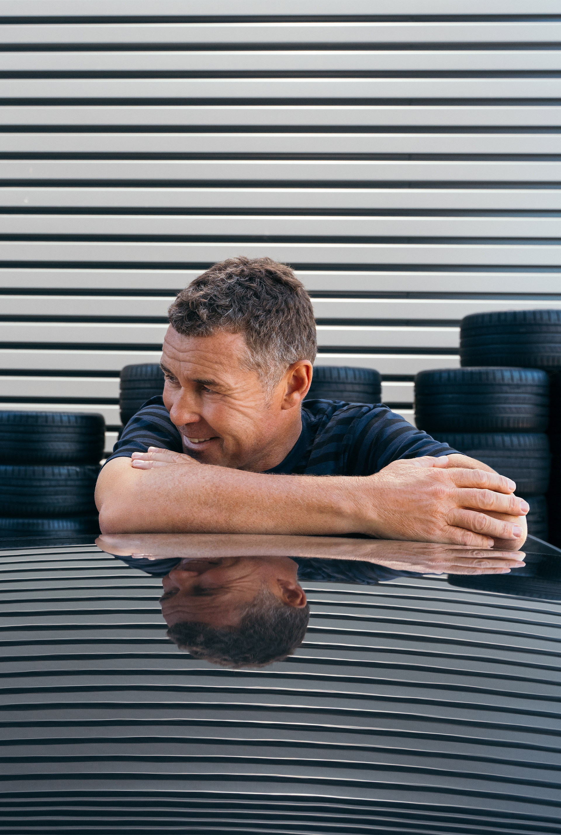 Tom Kristensen se penche en arrière sur la voiture de manière détendue, avec un sourire en coin.