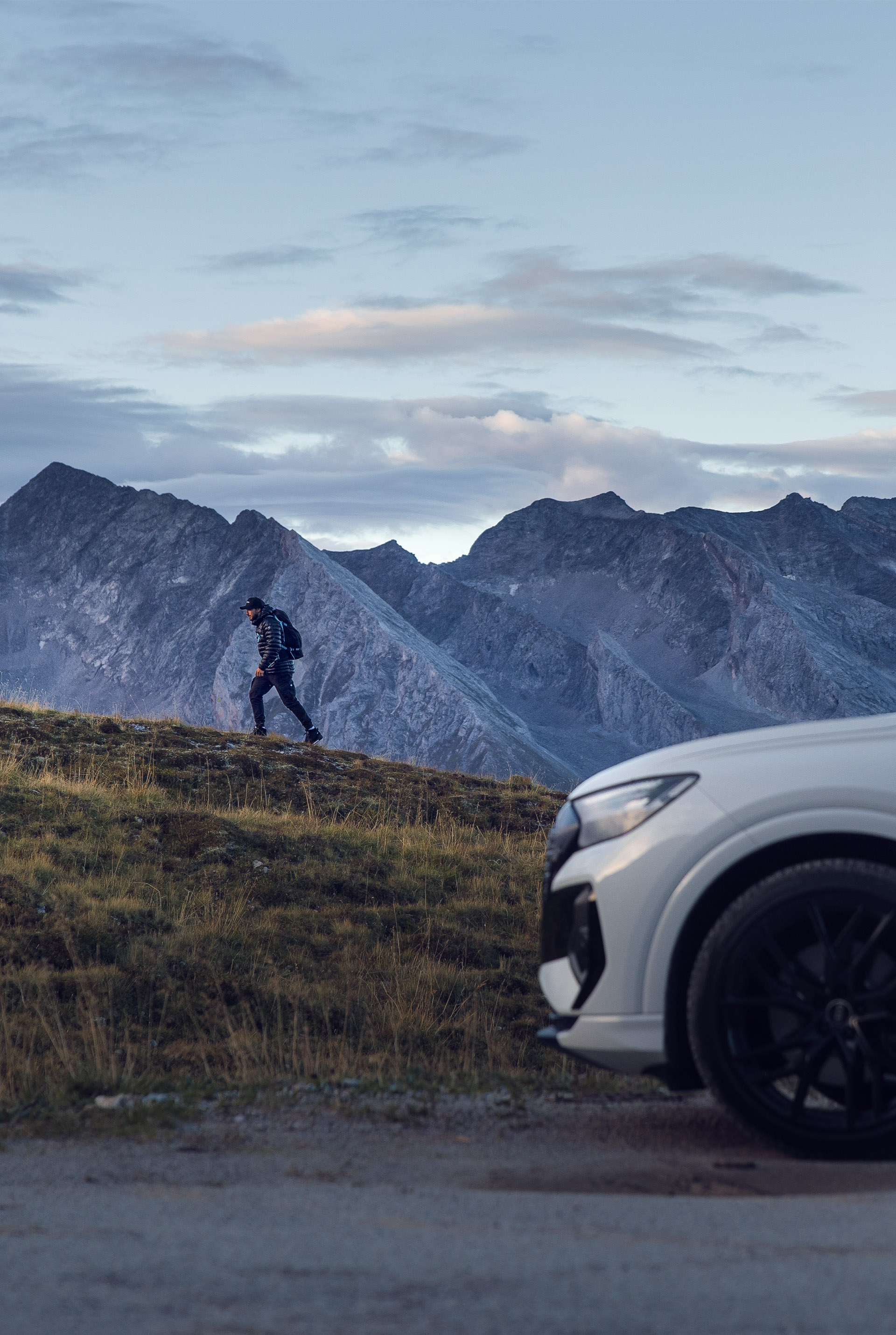 De witte Audi Q4 e-tron staat voor een berg waar Tom Klocker naar boven wandelt.